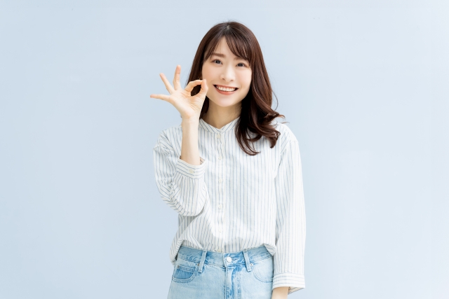 若い女性が笑顔で人差し指と親指で丸のサインをしていえる。他の指は立てている