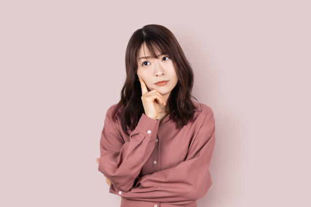 若い女性が頬に人差し指をあてて考え事をしていえる。