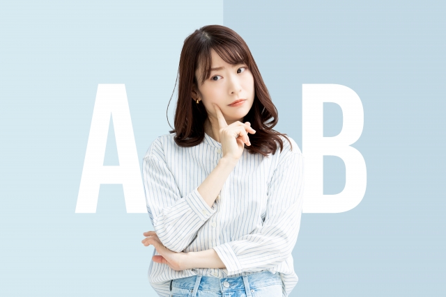若い女性が頬に人差し指を頬にあててどちらを選ぶべきか考えている