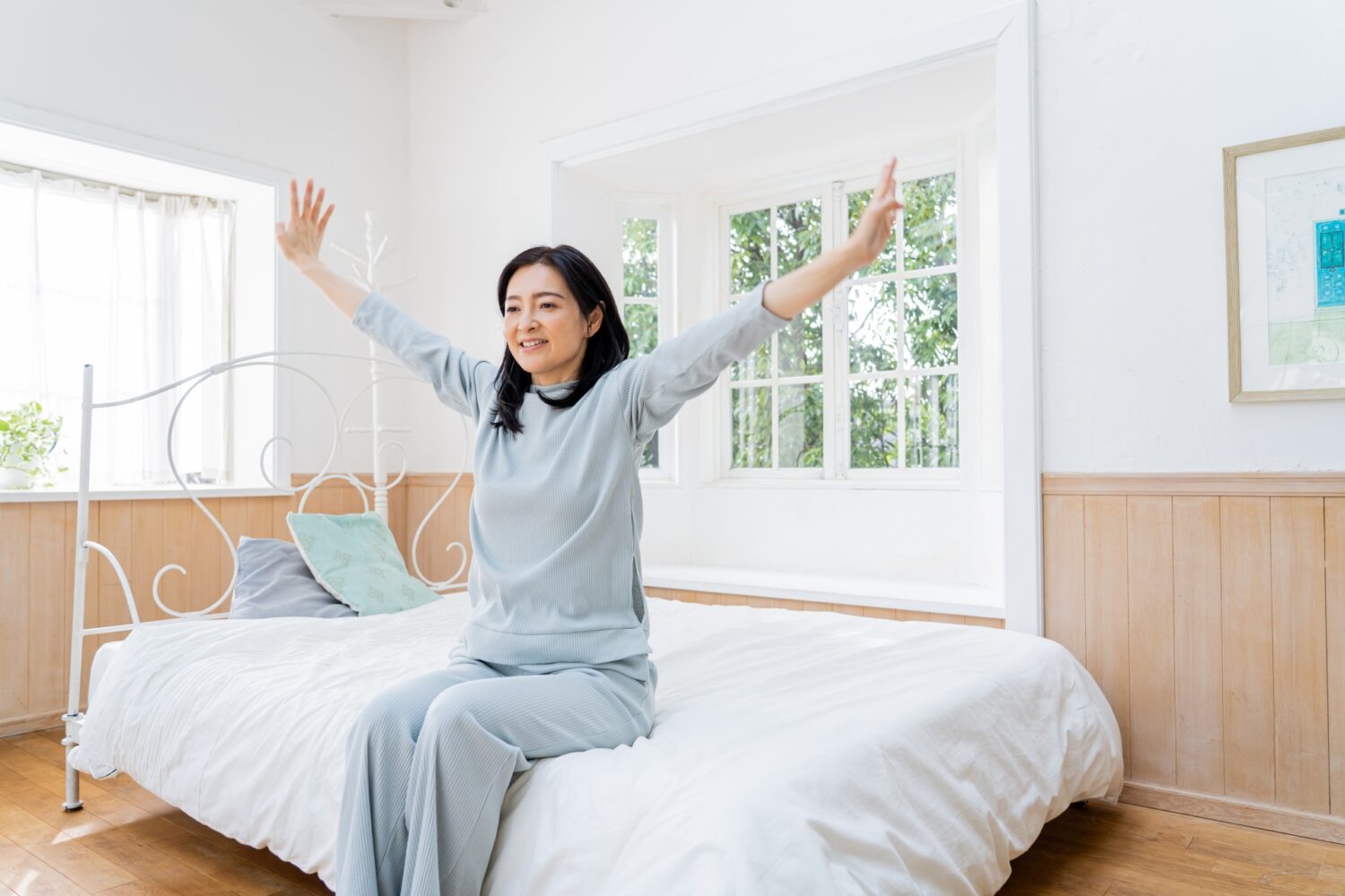 ベッドの端に座りながら両手を上に広げている女性